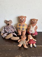 Five vintage rustic country charm dolls displayed on dark wooden surface against white wall.