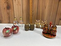 Five sets of vintage salt and pepper shakers including apples, light bulbs, owls, and a matryoshka set on wooden surface with ruler for scale.