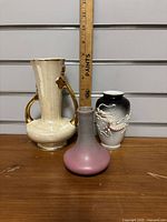 Front view of three vintage vases showing decorative details and scale with ruler.