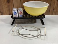 Yellow Pyrex large mixing bowl, two vintage milk glass salt and pepper shakers, and metal casserole dish carrier on a white surface with wood panel background