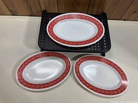 Three oval Pyrex platters arranged on a white surface and black perforated shelf, showing overall design and size comparison.