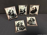 Group of five vintage silhouette artworks on glass with paper frames on dark surface. Shows wear on frames and clear glass condition.