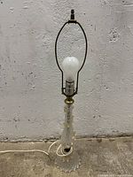 Full view of entire lamp showing clear bubble textured glass base and brass fittings, with bulb and harp.