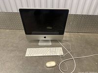 Photo of an Apple iMac desktop with a wired keyboard and mouse on the floor against a wall.