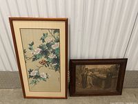 Two framed artworks placed next to each other against a vertical metal surface, showing floral bird painting and a vintage cityscape print.