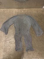 Full view of the metal chainmail armour shirt laid flat on a concrete surface, showing the entire shirt including sleeves and front lower split.