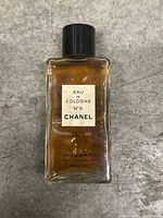 Clear photo of vintage rectangular glass bottle of Chanel N°5 Eau de Cologne perfume with black screw cap and original label, placed on a gray surface.