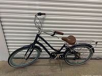 Full side view of the blue cruiser bike showing the frame, brown seat, handlebar grips, and tires with blue accents.