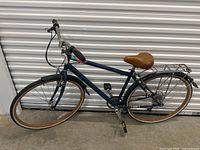 Full side profile of the blue cruiser bike showing the frame, saddle, tires, and rear rack.