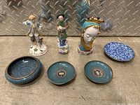Front view of all ceramic figurines and plates arranged on concrete surface.