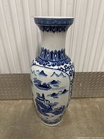 Front view of tall blue and white porcelain vase with landscape and floral patterns on white background