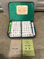 Open green-lined carrying case showing Mah Jong tiles, chips, two rule booklets, and label inside lid.