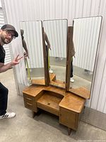 Mid century modern wooden dresser vanity with trifold mirror and drawers seen with person next to it
