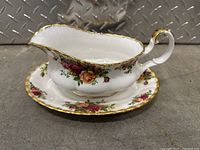 Gravy boat with ornate handle and matching underplate featuring floral design and gold trim, view from front.