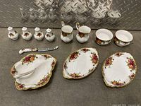Full view of the Royal Albert Old Country Roses porcelain set showing condiment shakers, creamers, plates, and spreading knife with floral patterns and gold trim.