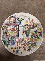 Front view of white porcelain plate with multicolored depiction of children performing dragon dance, firecrackers and architectural motifs against mountain backdrop