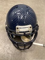 Front view of navy blue Seattle Seahawks football helmet with black face mask and SEAHAWKS label.