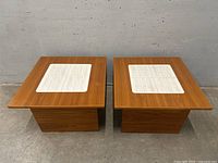 Pair of square teak side tables viewed from the front, showing wood grain and tile inlay on top.