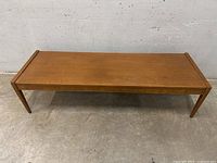 Full view of the rectangular teak coffee table showing the tabletop and legs.