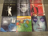 Photo showing six vinyl record albums stacked, including Alice Cooper with makeup close-up, Sade 'Promise', Steve Martin, Tom Petty & The Heartbreakers, The Beach Boys 'Endless Summer', and one with a man and horn artwork.