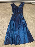 Blue satin sleeveless vintage dress laid flat on carpet, showing front detail and pleated skirt