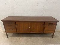Front view of walnut mid-century modern credenza showing drawers, filing cabinet drawer, and sliding doors.