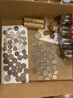 Wide view of mixed coins, coin tubes and glass jars in box
