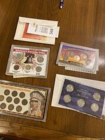 Top view of four coin collections including Two Centuries of Indian Pennies, Wild West Coin Collection, The First State Quarters of the 21st Century, and America's Favorite Coins sets, all in display cases or envelopes.