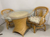 Full set view showing round glass top table and two bamboo swiveling chairs with cushions.