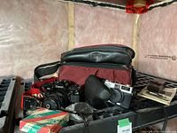 Wide shot of Canon A-1 camera, Minolta Hi-Matic camera, Baby Splicer box, leather Canon case, maroon carrying case, and accessories on shelf