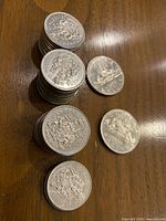 Stacked thirty-two 50 cent coins and two 2 dollar coins displayed on wooden surface, showing the coat of arms side for 50 cents and the canoe design for 2 dollars.
