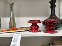 Shelf with tall multicolor ceramic vase, large black and red vase, red pedestal dishes, and a decorative plate