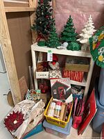 Overview of lot items on shelving including ceramic trees, artificial tree, wrapping supplies, book and ornaments