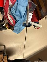 Épée fencing sword with metal guard laid across folded flags, plastic bag of metal badges visible.