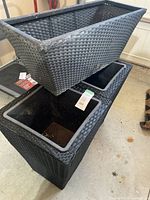 Black wicker-look outdoor planters showing rectangular and tall designs with plastic liners inside.