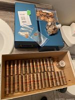 Two blue metal boxes on counter with loose pennies and a cardboard tray of penny rolls