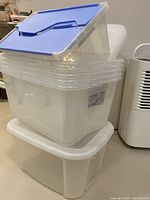 Stack of six clear plastic storage bins with five blue lids and one extra bin with flipped blue lid.