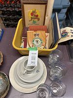 Overview of stacked porcelain RCAF dishes, cup and clear glass cups next to yellow bin of ephemera