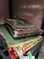 Stack of vintage scrapbooks with worn leather and fabric covers and aged paper pages