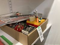 Sewing supplies arranged in a cardboard box on a shelf, showing pins, scissors, and thread bobbins.