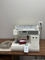 Full front view of sewing machine on tabletop with red tool chest beside it and clear bobbin case