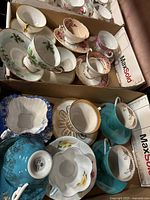 View of multiple assorted vintage teacups and saucers in cardboard boxes showing floral and gold trim patterns.