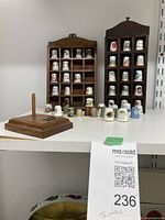 Two wooden racks filled with metal, China, and Wedgewood thimbles, along with a wooden single thimble stand in front