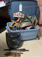 Overview of plastic tote filled with hand tools and two knives in front