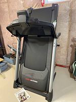 Folded treadmill showing running deck, frame and manuals at base