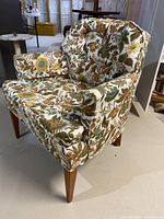 Front right angle view of floral tub chair showing fabric pattern, tufted backrest, and oak tapered legs.