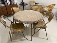 Full set showing round card table with laminate top and four folding chairs with beige marbled vinyl upholstery, metal frames in bronze tone.