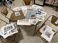 Table with a spread of various unframed prints and cards showing colorful illustrations including bird prints and city landmarks.