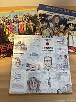 Three Beatles-related vinyl record albums displayed overlapping on a wooden surface.