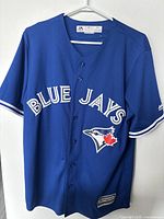Front view of blue Blue Jays Majestic baseball jersey with button-up style, team lettering and logo visible.